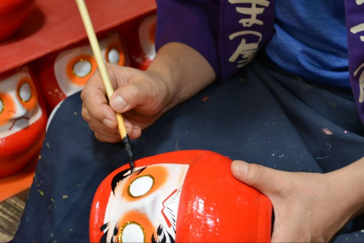A craftsman painting the eyebrows onto a Daruma doll